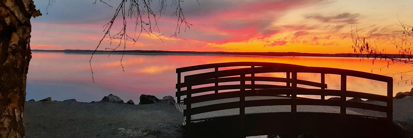 Pieni puinen silta Näsijärven rannalla, taustalla auringonlaskun punertama taivas.